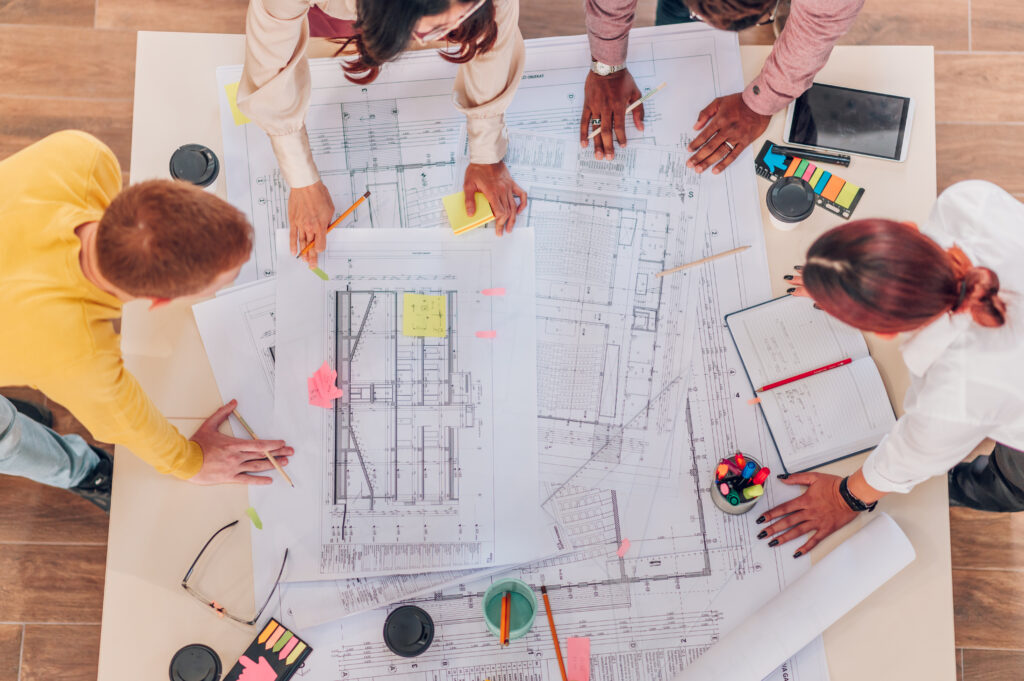 Four people stand around a table covered with blueprints and notes, discussing specialty tax services for architectural projects.
