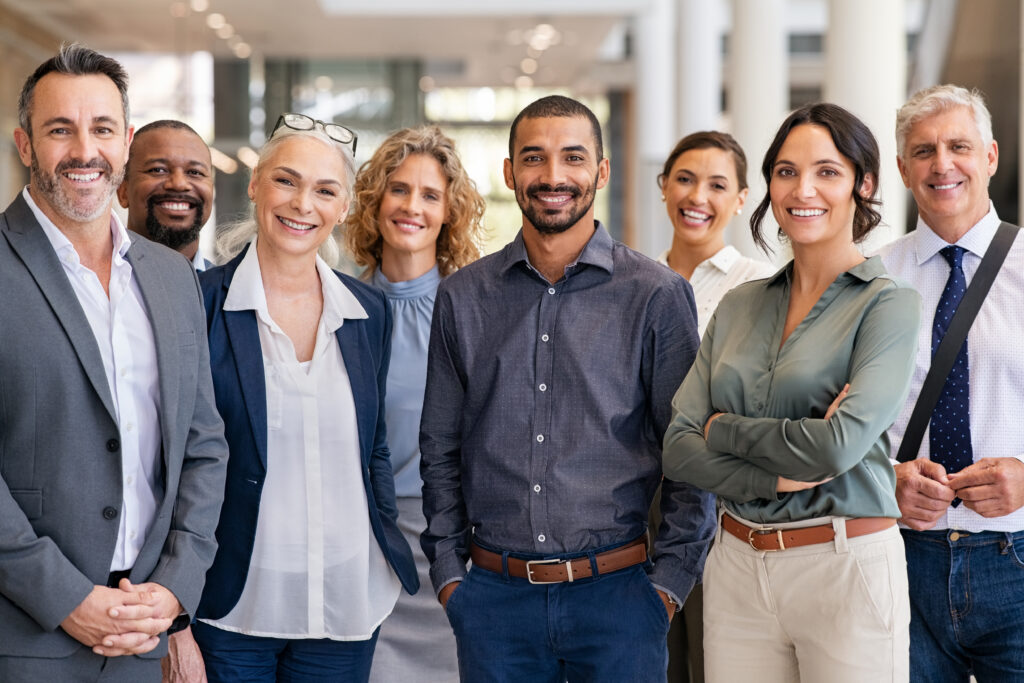 A group of eight professionally dressed people stand indoors, smiling and representing specialty tax services for professionals.